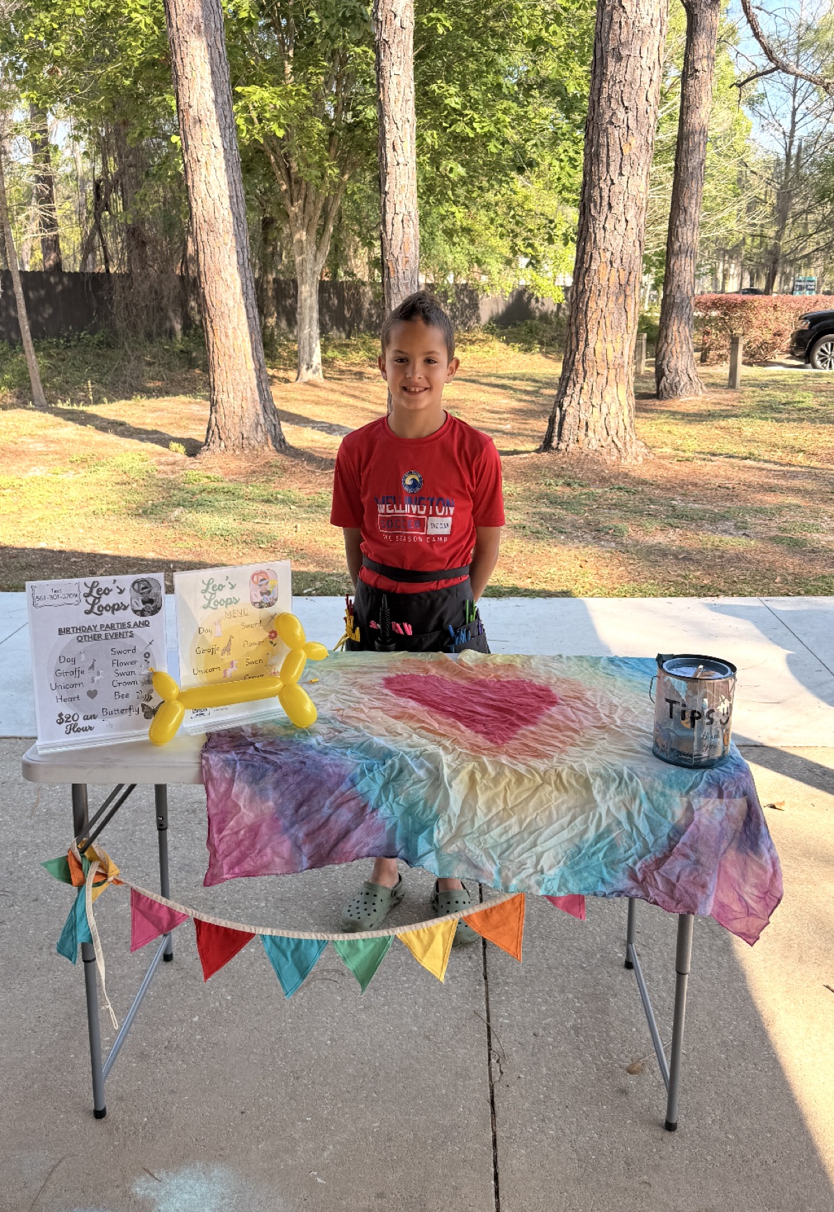 Leo standing behind his balloon table at a park.